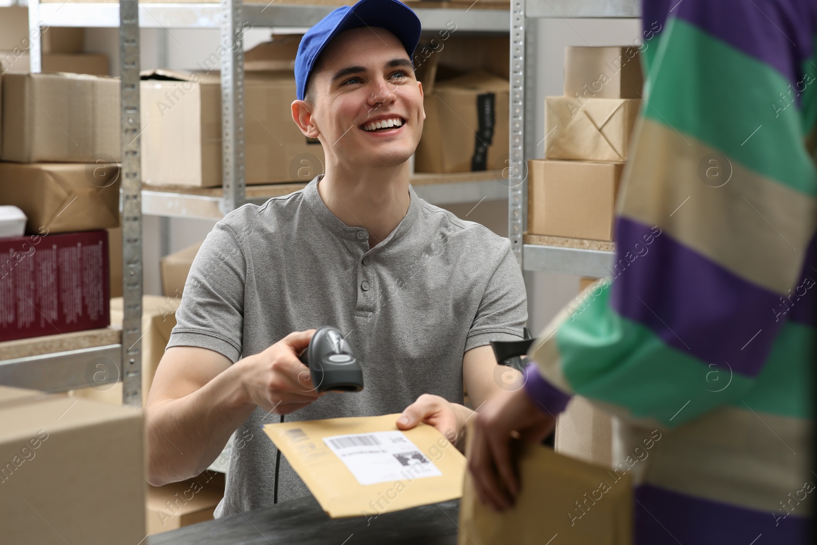 Photo of Woman and post office worker with scanner reading parcel barcode at table indoors