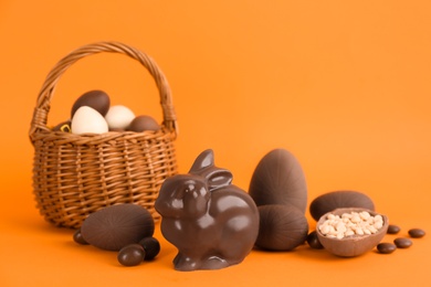 Photo of Chocolate Easter bunny, eggs and candies on orange background. Space for text