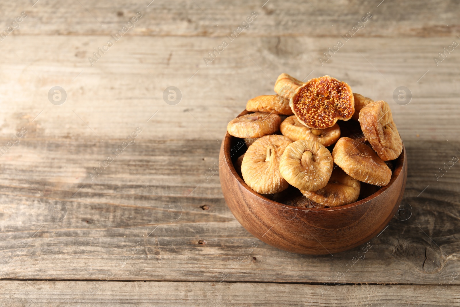 Photo of Bowl with tasty dried figs on wooden table. Space for text