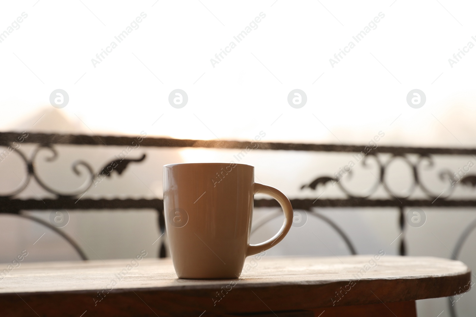 Photo of Cup of hot tea on wooden table at balcony