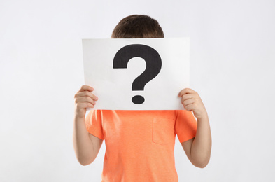 Photo of Little boy holding paper with question mark on white background