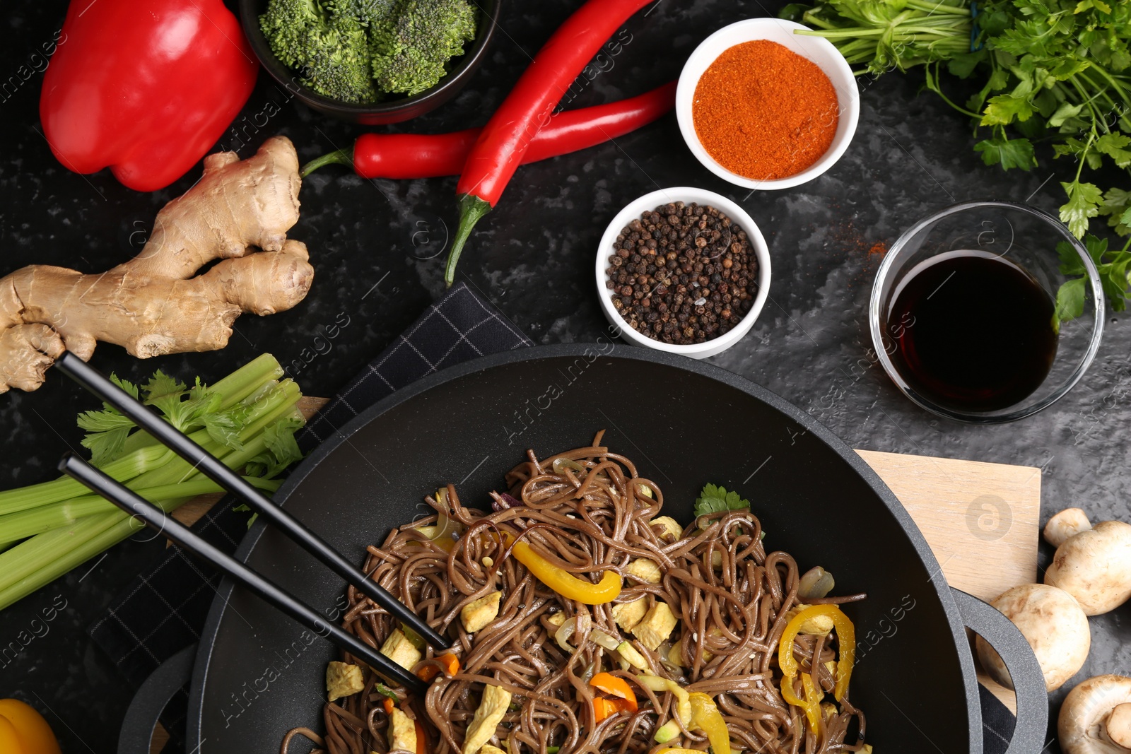 Photo of Stir-fry. Tasty noodles with meat and vegetables in wok served on dark textured table, flat lay