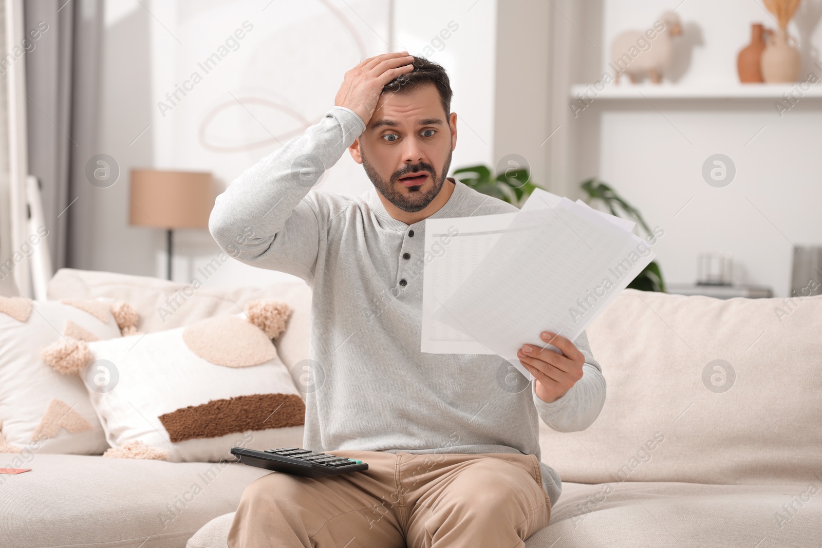 Photo of Shocked man with debt notifications and calculator planning budget at home. Financial problem