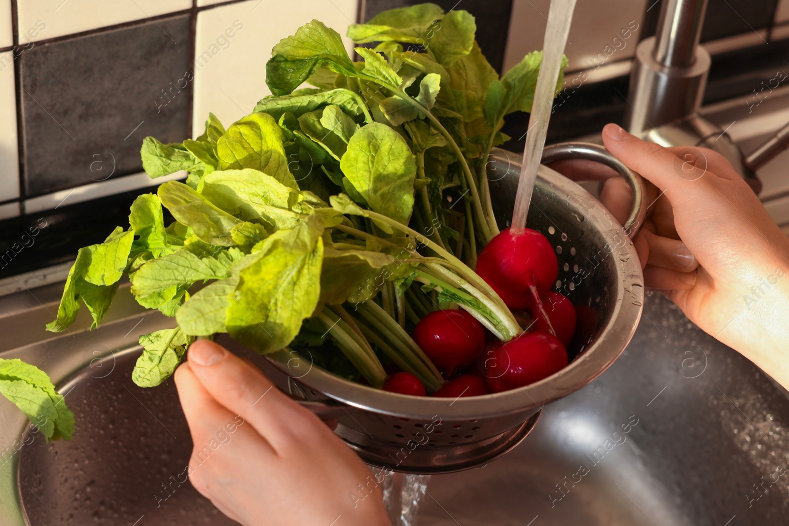 Photo of Woman washing fresh radishes in metal colander, closeup