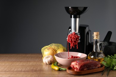 Photo of Electric meat grinder with minced beef and products on wooden table against dark background. Space for text
