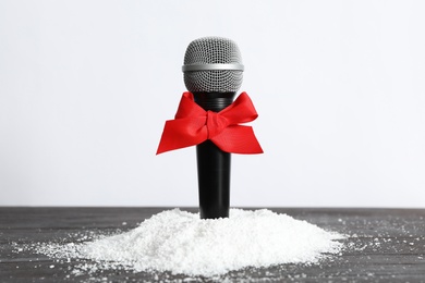 Photo of Microphone with red bow and snow on wooden table against white background. Christmas music