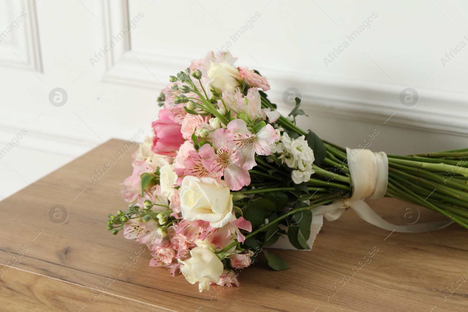 Photo of Beautiful bouquet of fresh flowers on wooden table near white wall