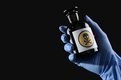 Photo of Woman in gloves holding glass bottle of poison with warning sign on black background, closeup. Space for text