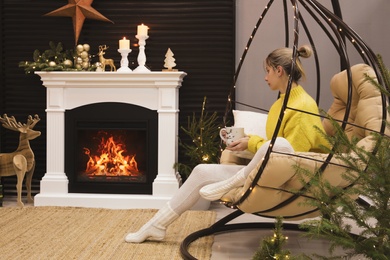 Photo of Woman with cup of drink sitting near burning fireplace
