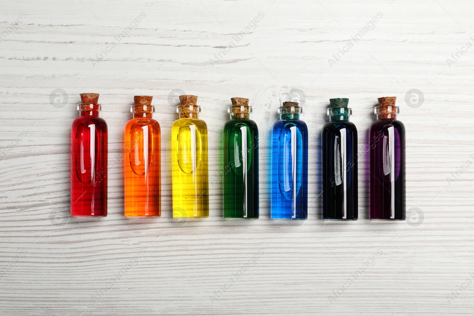 Photo of Glass bottles with different food coloring on white wooden table, flat lay