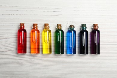 Glass bottles with different food coloring on white wooden table, flat lay