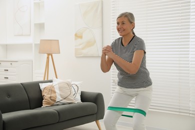 Photo of Senior woman doing squats with fitness elastic band at home