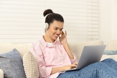 African American woman in headphones working on laptop in room