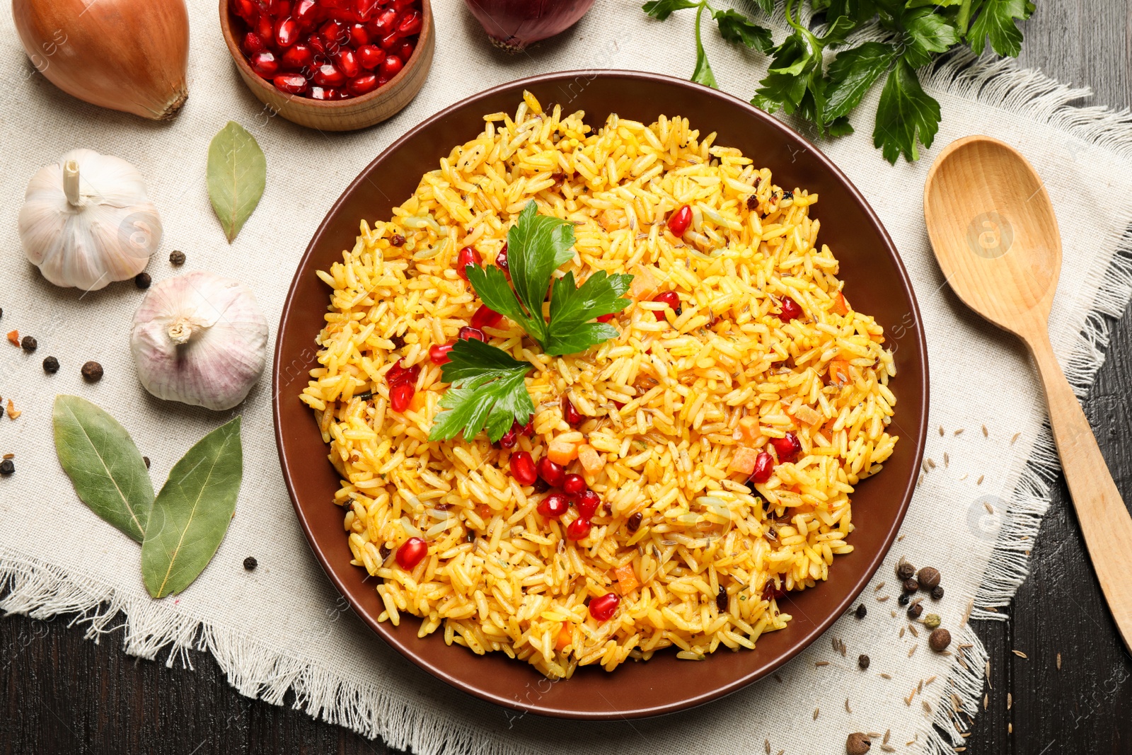 Photo of Tasty rice pilaf with pomegranate grains served on black wooden table, flat lay