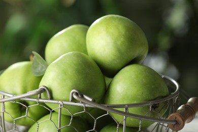 Metal basket with ripe green apples on blurred background, closeup