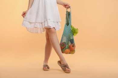 Woman with string bag of fresh vegetables on beige background, closeup