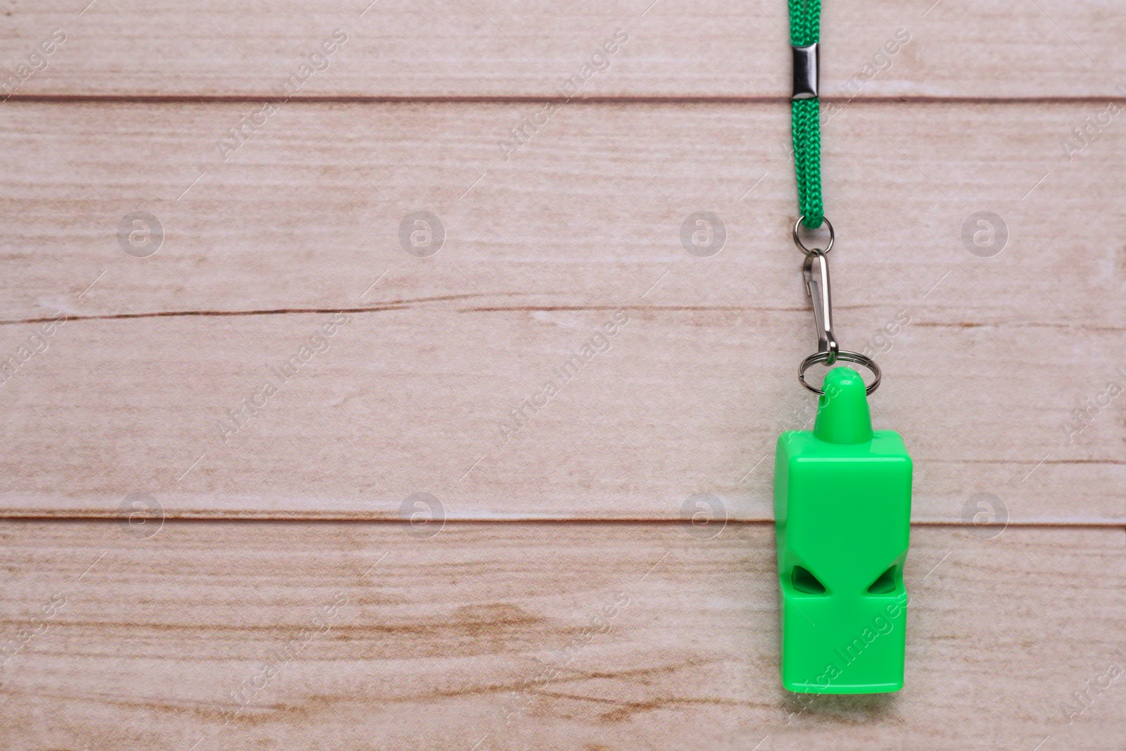 Photo of One green whistle with cord on light wooden table, top view. Space for text