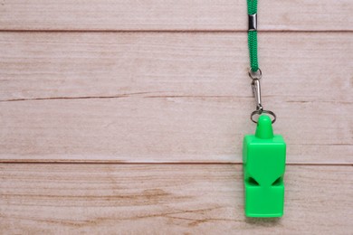 One green whistle with cord on light wooden table, top view. Space for text