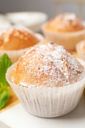 Tasty muffin powdered with sugar on table, closeup