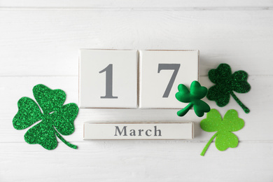 Block calendar and clover leaves on white wooden background, flat lay. St. Patrick's Day celebration