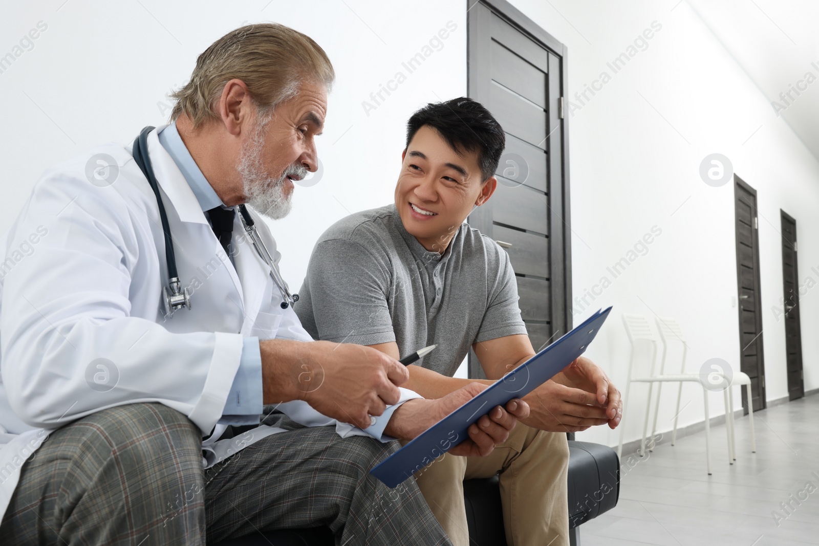 Photo of Senior doctor with clipboard consulting patient in clinic