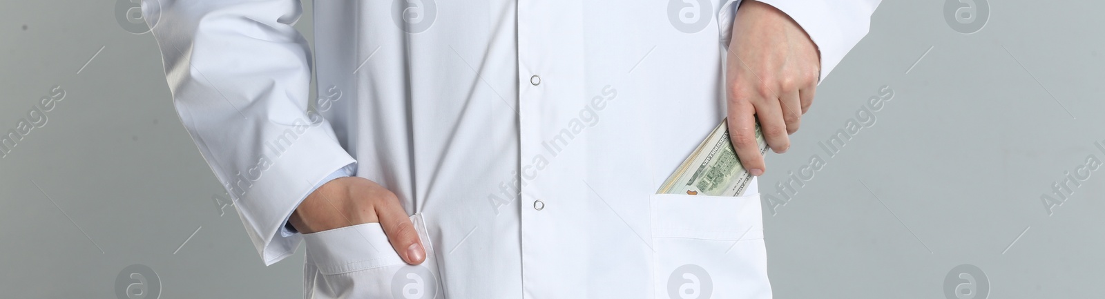 Image of Doctor putting bribe into pocket on grey background, closeup. Banner design