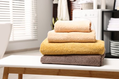 Photo of Stack of clean towels on white table in laundry room, space for text