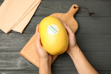 Woman holding ripe spaghetti squash on wooden table, top view