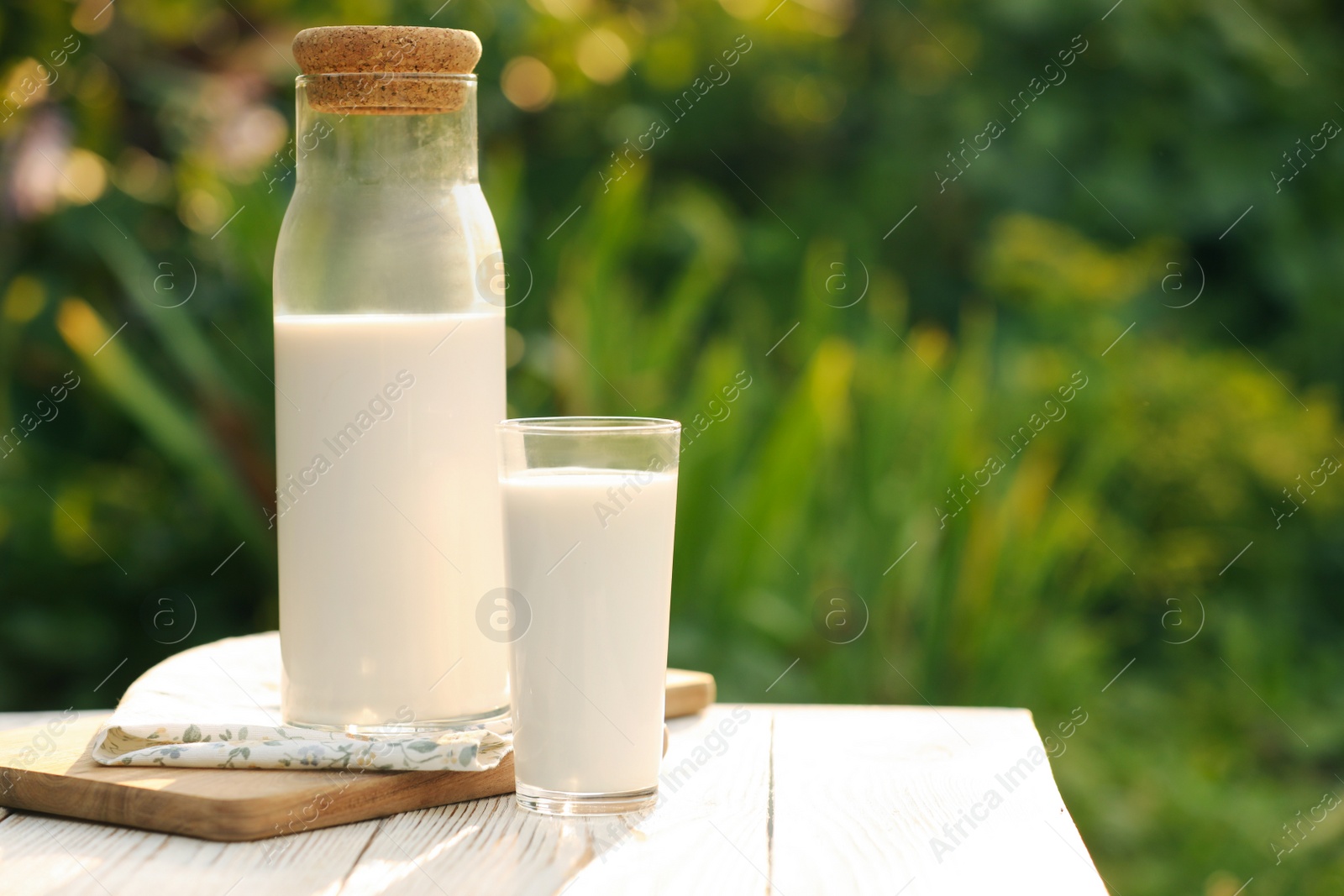 Photo of Bottle and glass of tasty fresh milk on white wooden table against blurred background, space for text