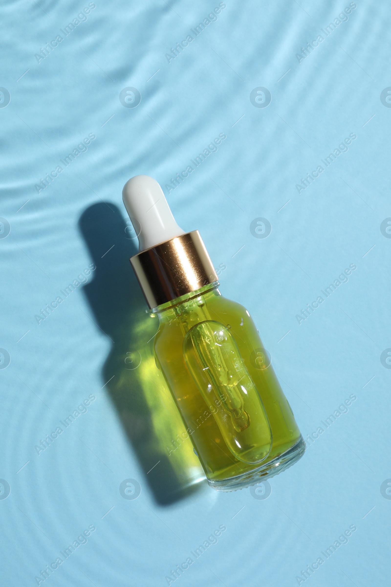 Photo of Bottle of cosmetic oil in water on light blue background, top view