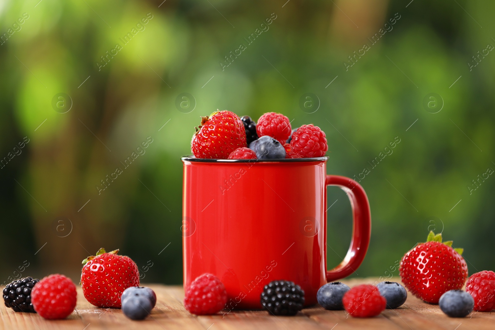 Photo of Mug with different fresh ripe berries on wooden table outdoors