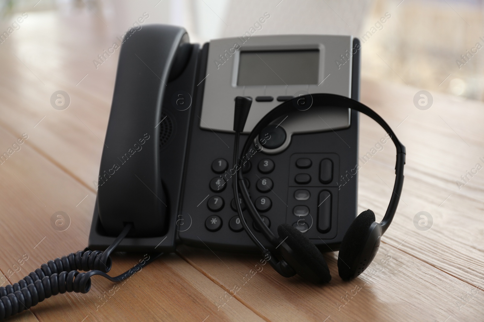 Photo of Office desktop telephone and headset on wooden table. Hotline service