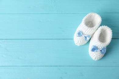 Handmade baby booties on wooden background, top view with space for text