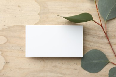 Blank business card and eucalyptus branch on wooden table, flat lay. Mockup for design