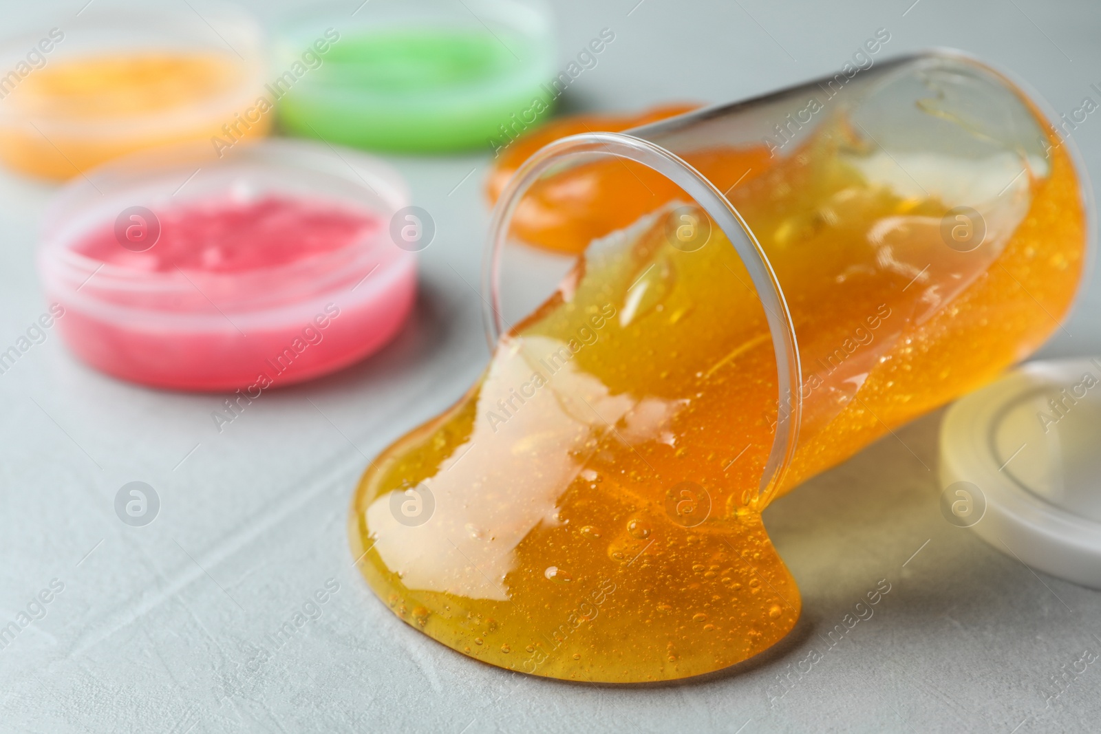 Photo of Overturned plastic container with orange slime on grey background, closeup