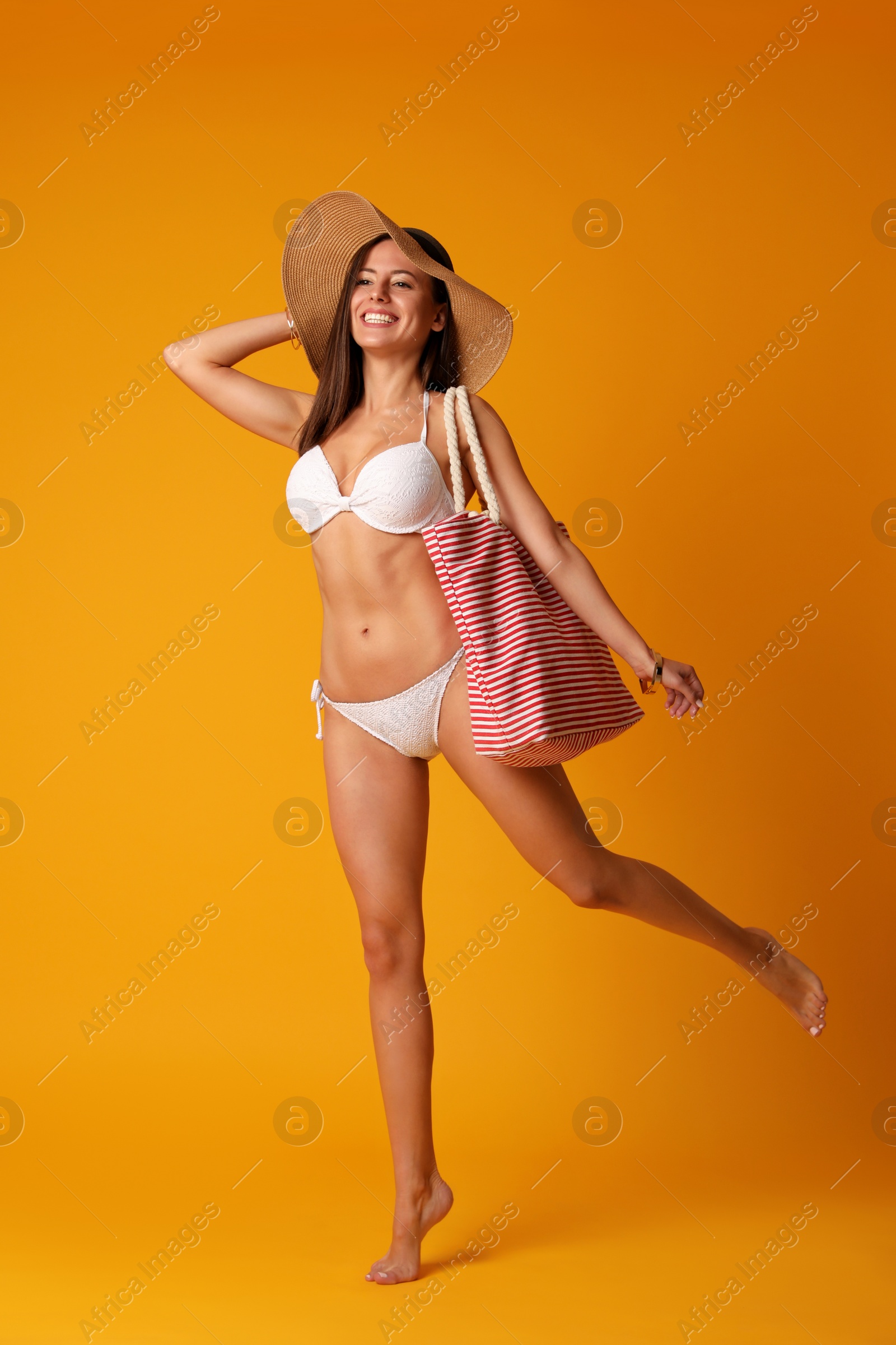 Photo of Pretty sexy woman with slim body in stylish white bikini on orange background