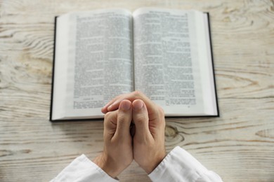 Photo of Man with Bible praying at white wooden table, above view