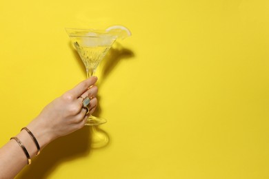 Photo of Woman holding martini glass of refreshing cocktail with lemon slice on yellow background, closeup. Space for text