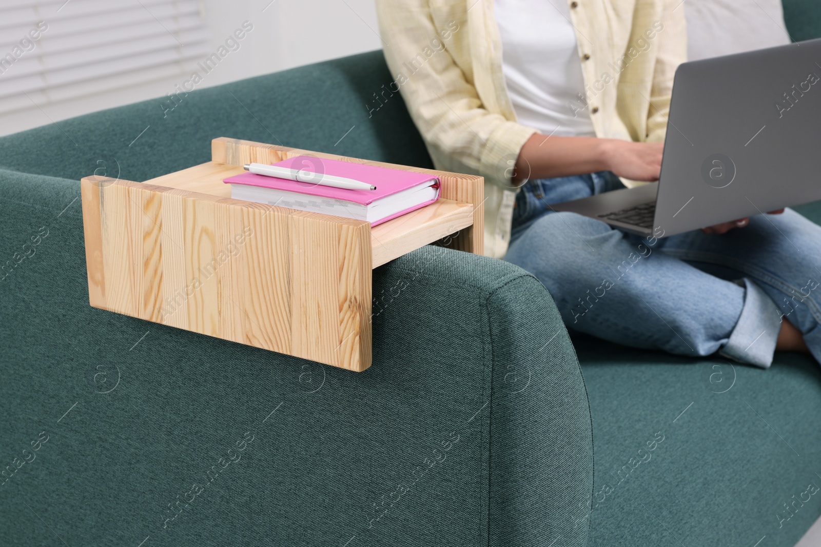 Photo of Notebook and pen on sofa armrest wooden table. Woman using laptop at home, closeup