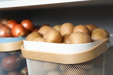 Photo of Baskets with potatoes and onions on shelf, closeup. Orderly storage