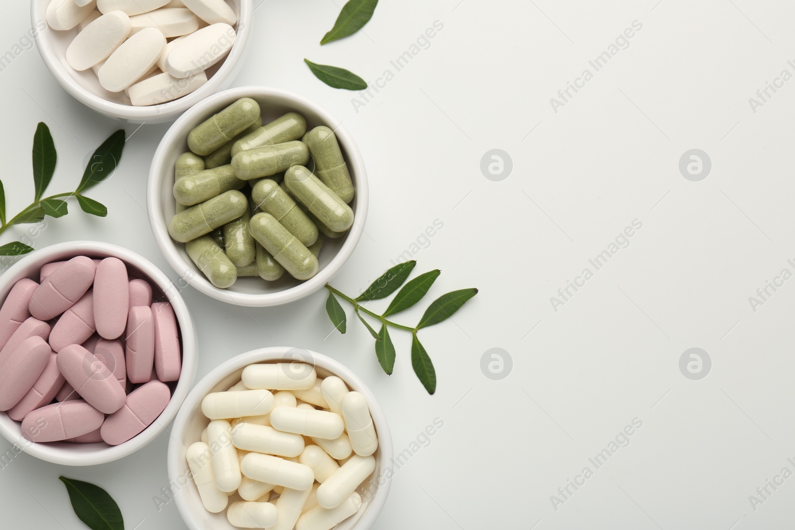 Photo of Different vitamin capsules in bowls and leaves on white background, flat lay. Space for text