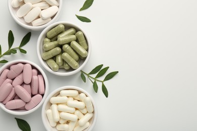 Different vitamin capsules in bowls and leaves on white background, flat lay. Space for text