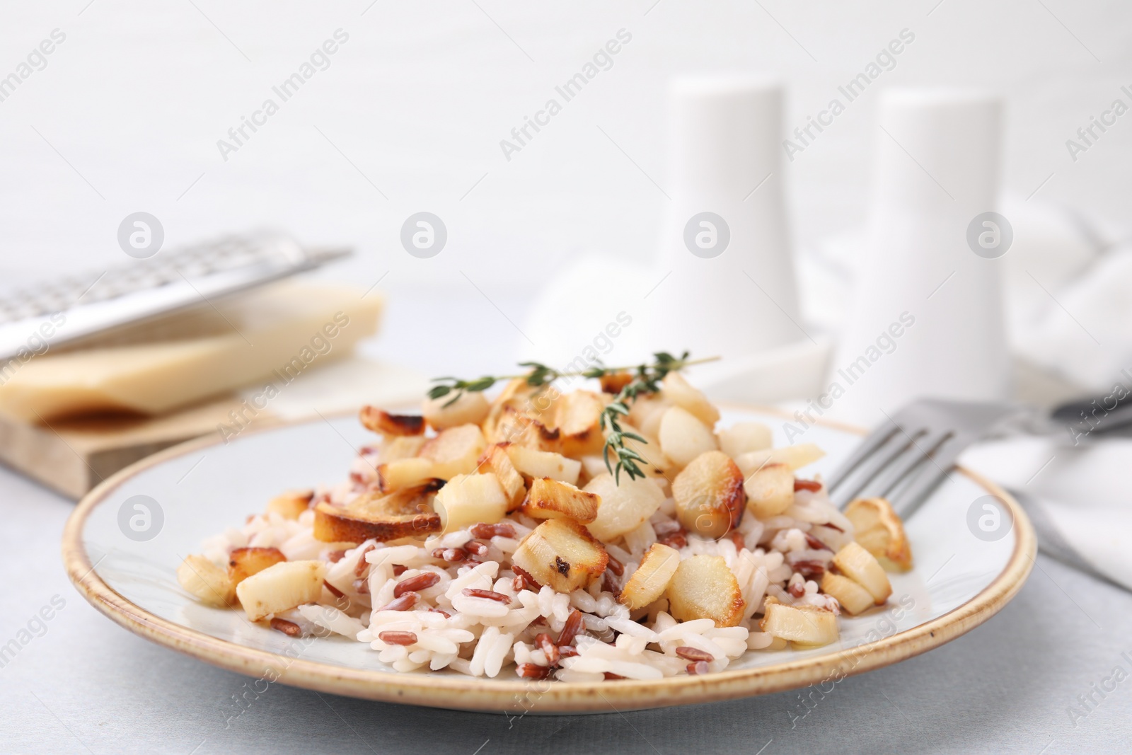 Photo of Plate with baked salsify roots, lemon, rice and fork on light grey table, closeup
