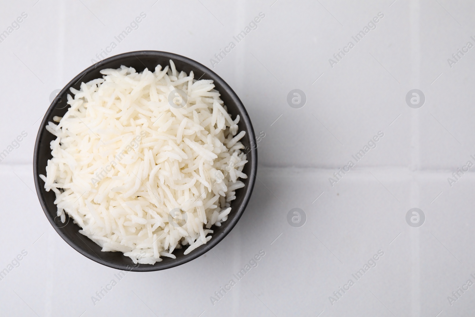 Photo of Bowl of delicious rice on white table, top view. Space for text