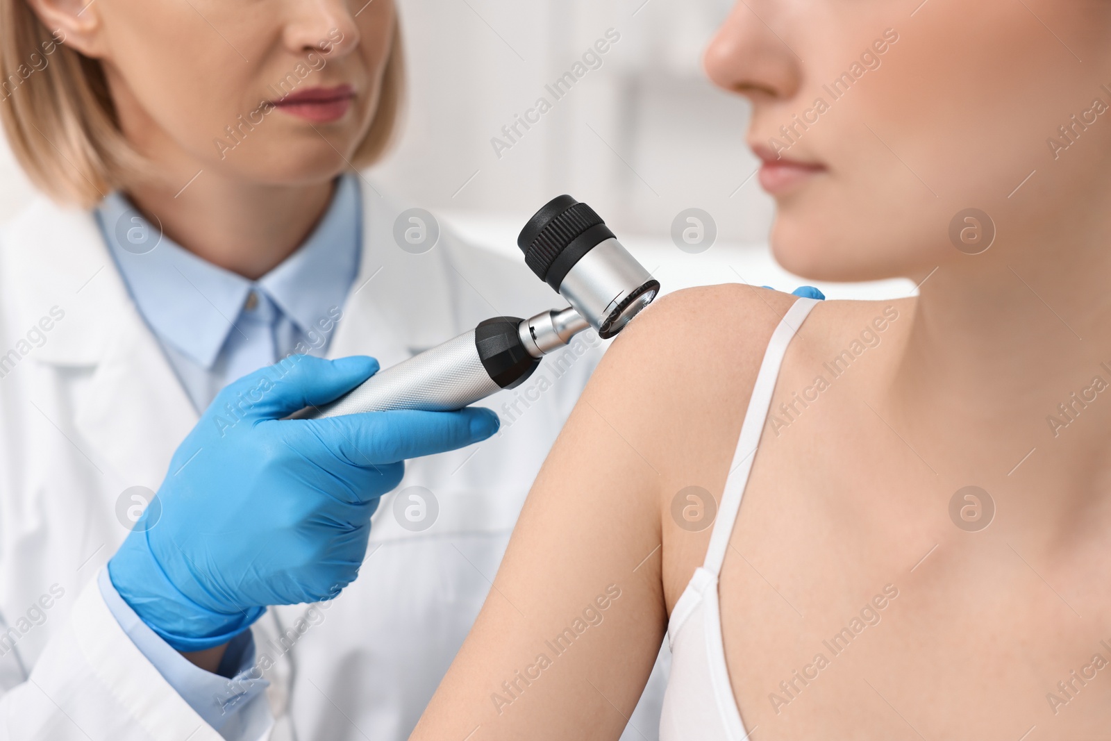 Photo of Dermatologist with dermatoscope examining patient in clinic, closeup