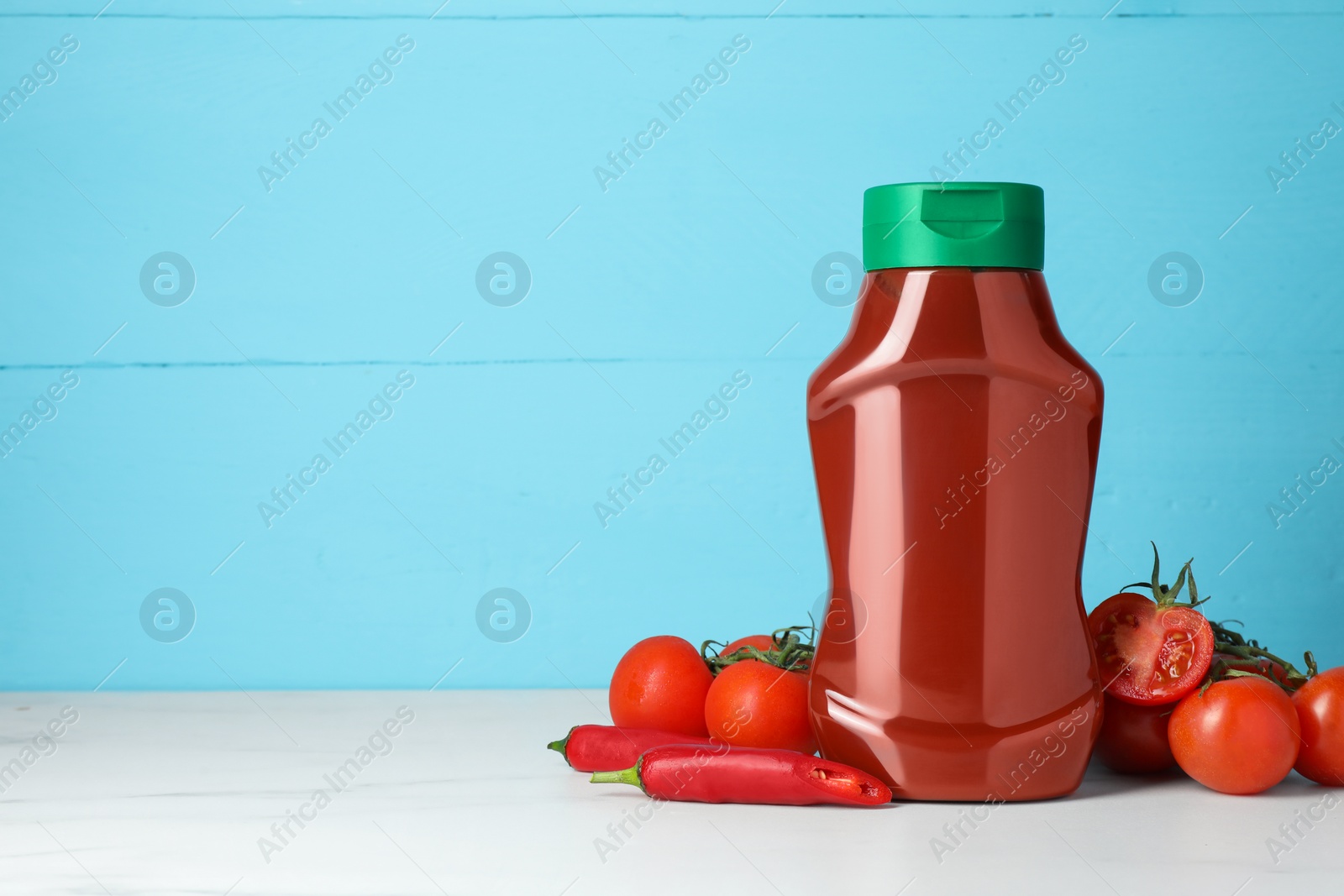Photo of Bottle of tasty ketchup and ingredients on white marble table. Space for text