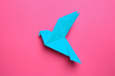Photo of Beautiful light blue origami bird on pink background, top view