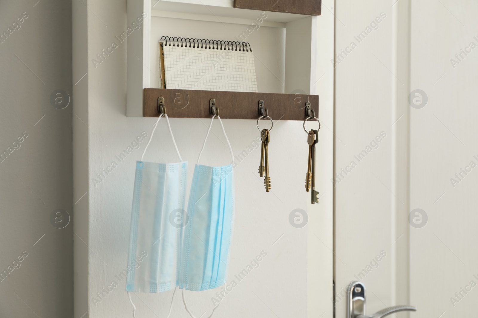 Photo of Hanger for keys with protective masks and notebook on shelf near door in hallway