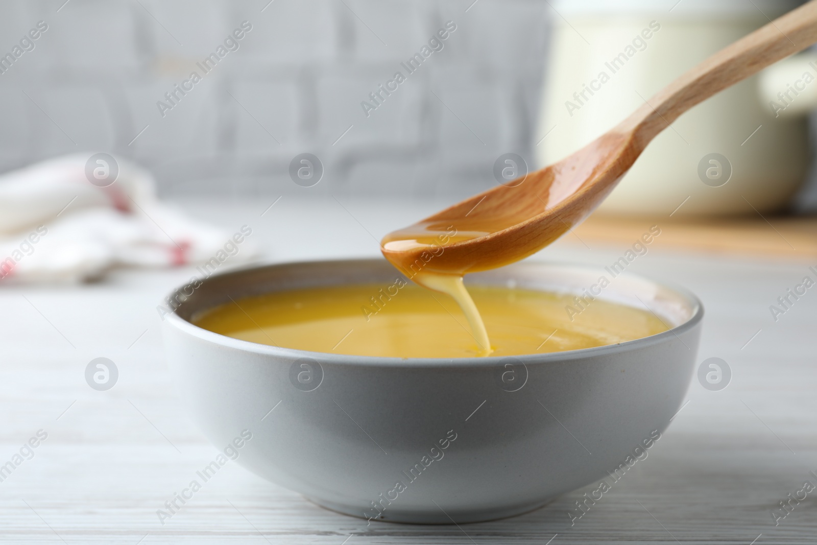 Photo of Spoon of clarified butter over bowl on white wooden table