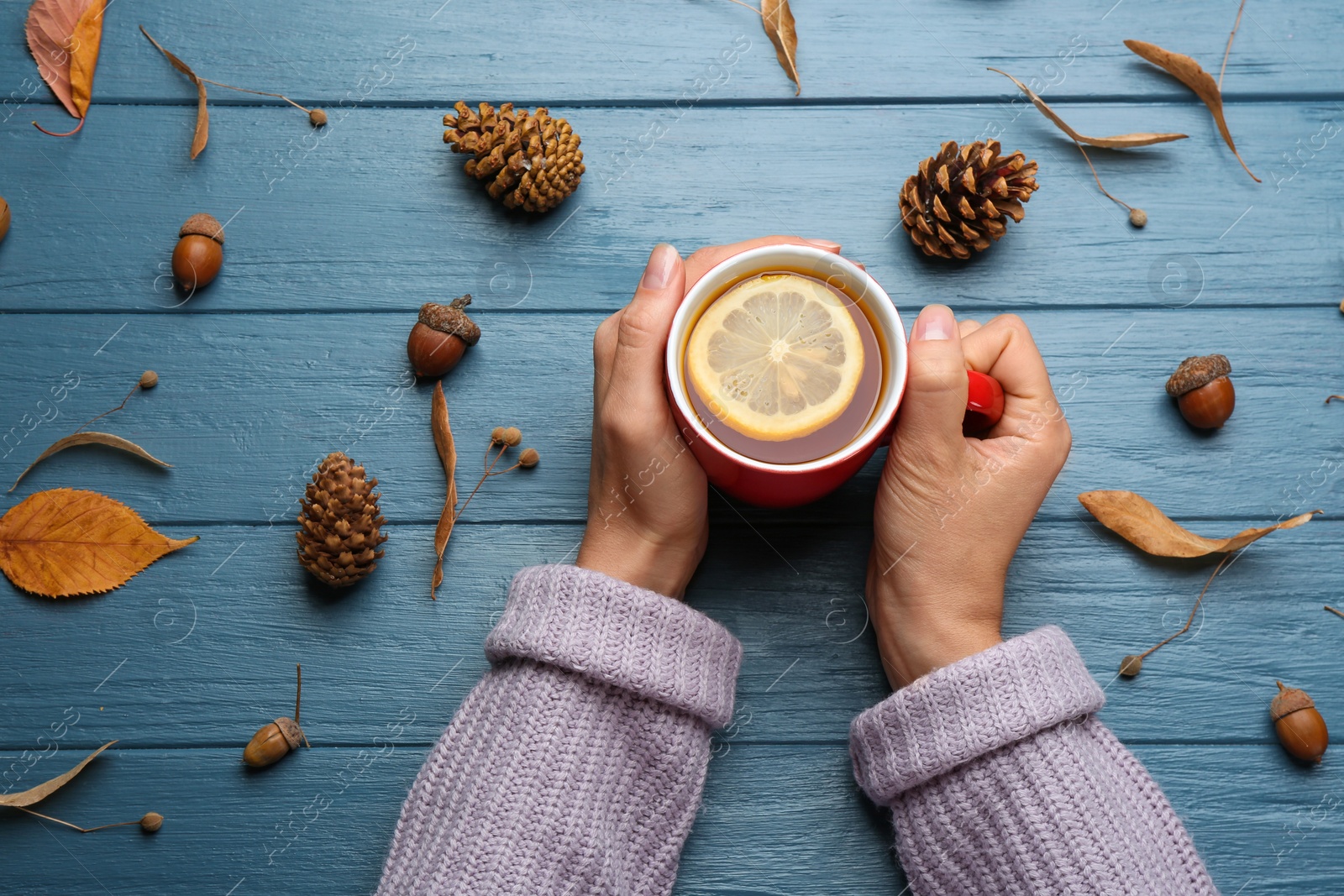 Photo of Woman with cup of hot drink at blue wooden table, top view. Cozy autumn atmosphere